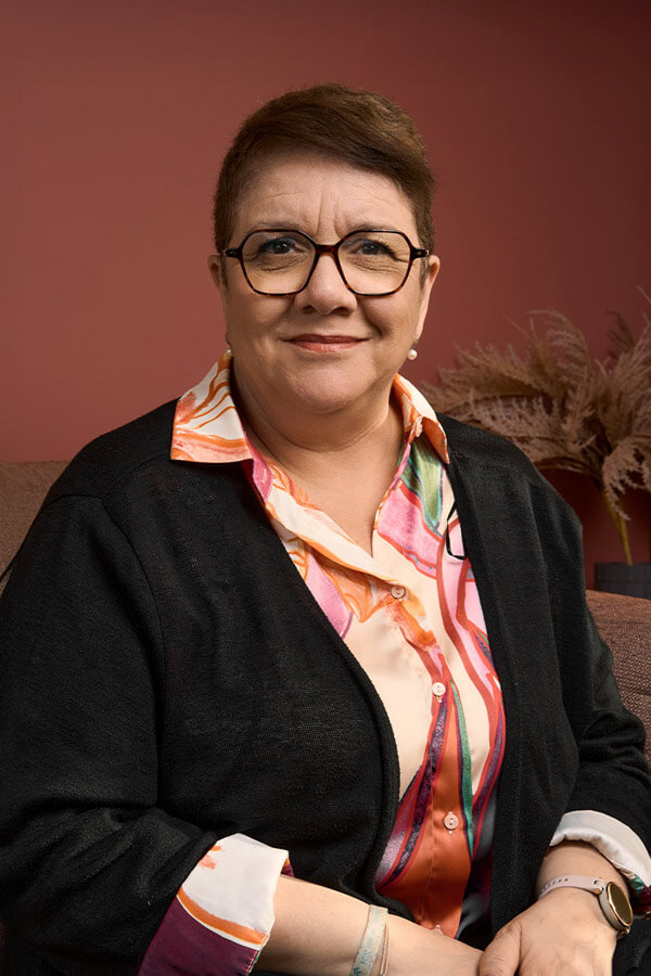 Portrait corporate d'une consultante souriante avec lunettes et chemisier à motifs colorés sur fond terracotta, Paris