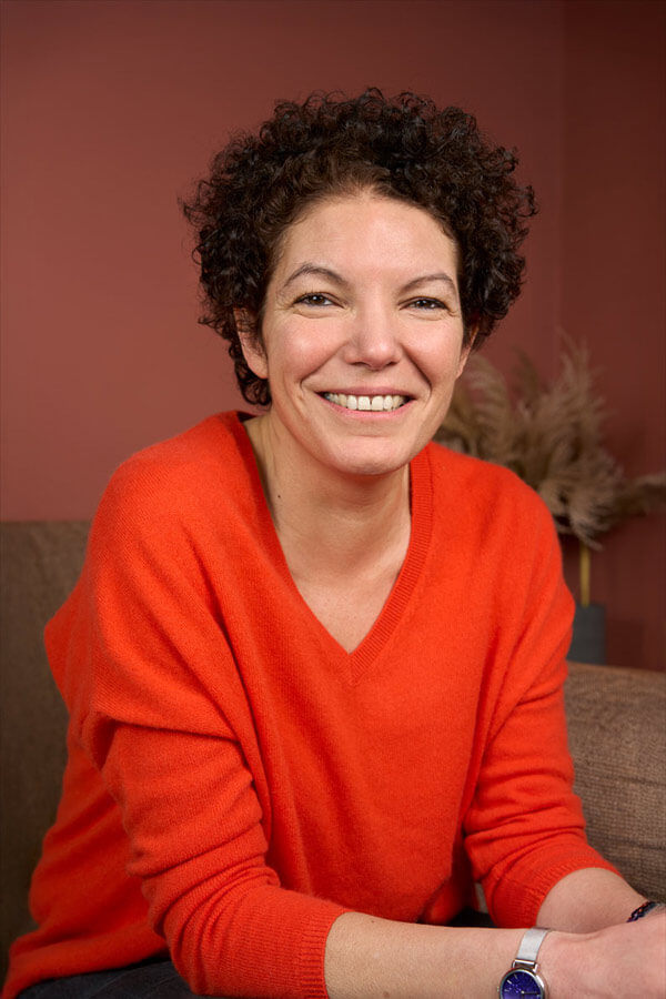 Portrait corporate d'une collaboratrice souriante en pull orange, en harmonie avec le fond terracotta, shooting Paris