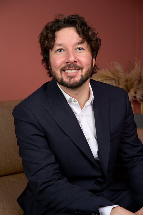 Portrait corporate d'un consultant souriant en costume bleu sur fond terracotta, cabinet de conseil Paris