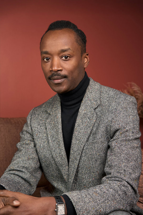 Portrait corporate d'un homme noir élégant en veste en tweed et col roulé sur fond terracotta, shooting Paris