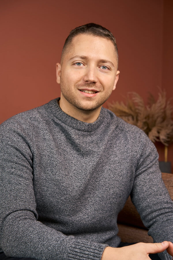 Portrait corporate d'un collaborateur en tenue décontractée (pull gris) sur fond terracotta, shooting équipe Paris